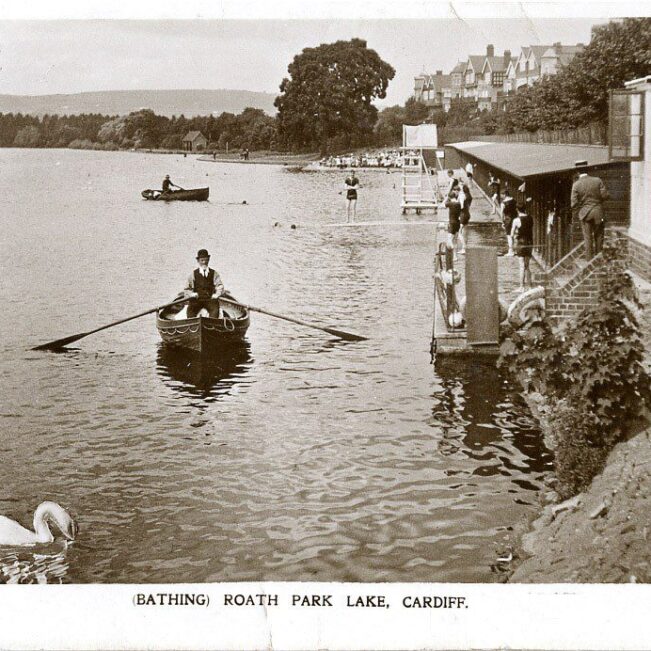 historic postcard showing bathing huts on Roath Lake with swimmers getting ready and a rowing boat passing by
