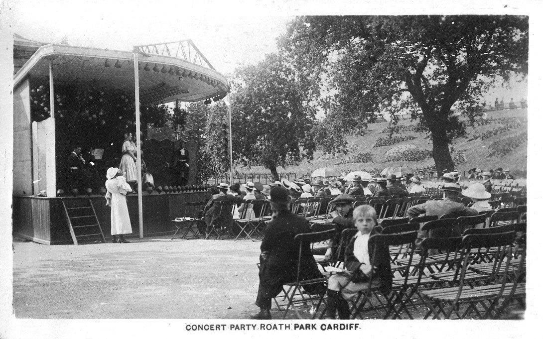 historic photo of a temporary stage in Roath Park with performers and a seated audience